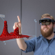 Ein Mann trägt eine VR Brille und zeigt mit dem Finger auf eine Grafik, die im Raum vor ihm erscheint.