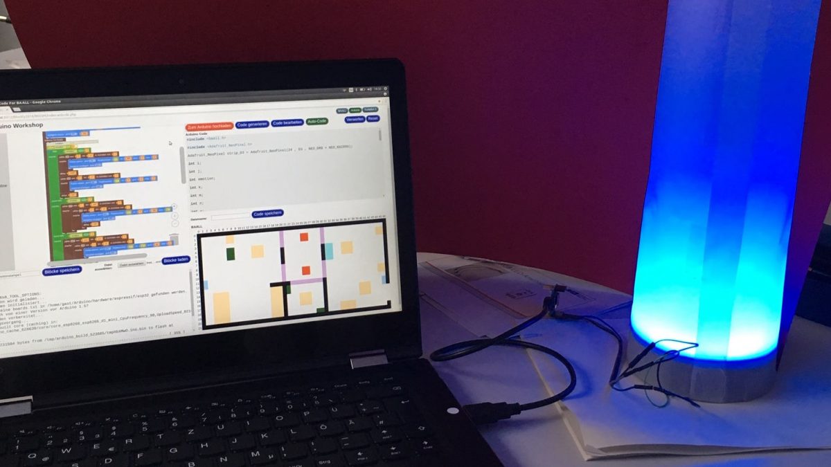 Auf dem Bild ist ein Laptop, der mit einer blau leuchtenden Lampe verbunden ist, zu sehen.